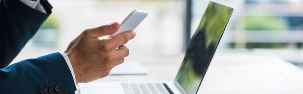 panoramic shot of man holding smartphone near laptop 