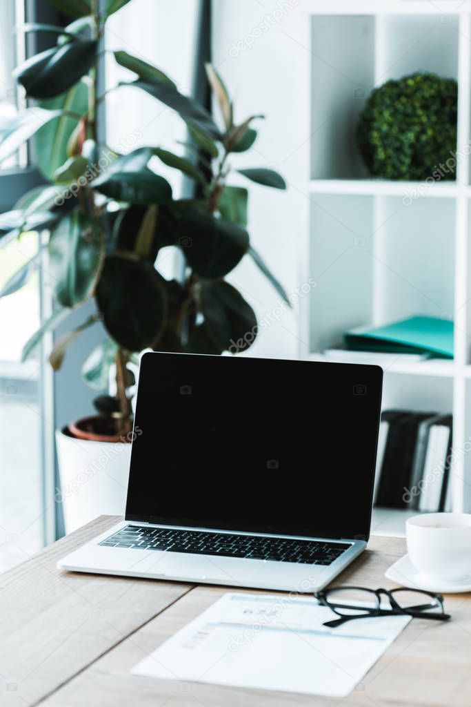 cup of coffee near glasses and laptop with blank screen on table 