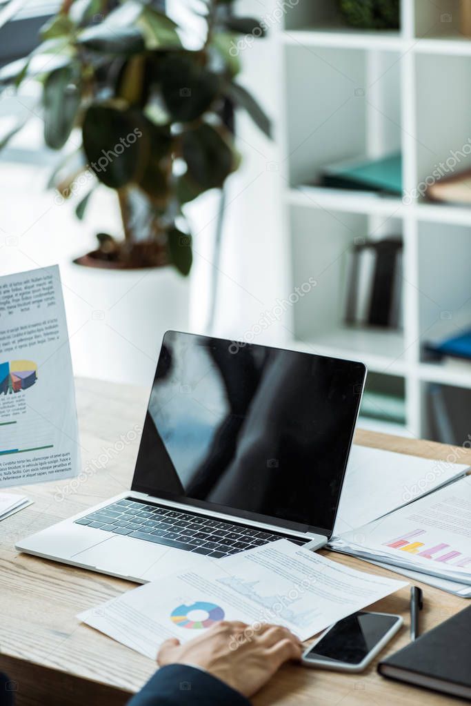 cropped view of businessman near laptop and smartphone with blank screens 