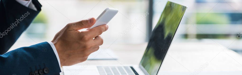 panoramic shot of man holding smartphone near laptop 