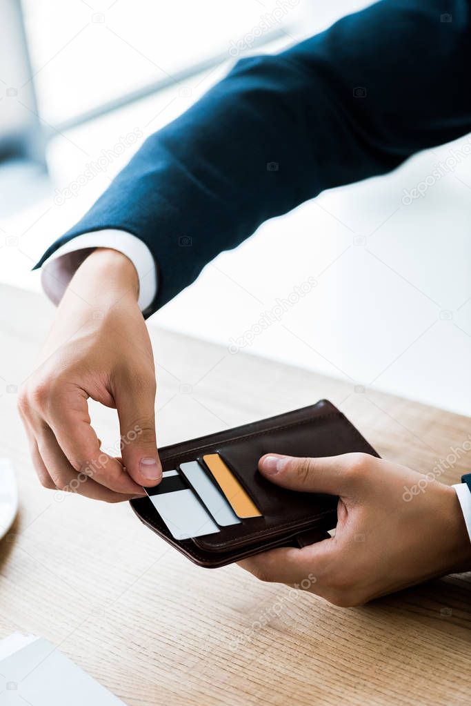 cropped view of businessman touching credit card while holding black wallet 