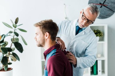 beyaz ceket ve gözlük sakallı chiropractor klinikte yakışıklı hastanın geri dokunmadan 