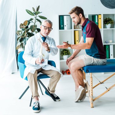 gözlük doktor yakınında omurga modeli bakarken yakışıklı sakallı adam gesturing 