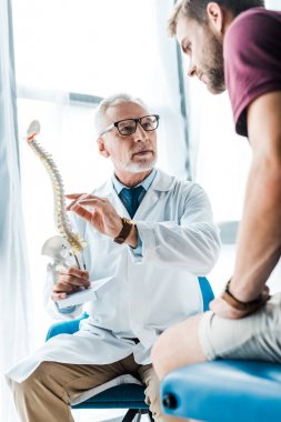 omurga modeli tutarken doktor gesturing yakınında oturan adam düşük açı görünümü 