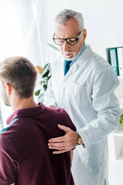 診療所で患者の背中に触れる白いコートの医者 — ストック写真