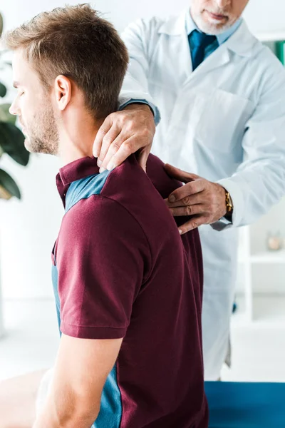 kapalı gözlü hastanın arkasına dokunan beyaz önlüklü chiropractor kırpılmış görünümü