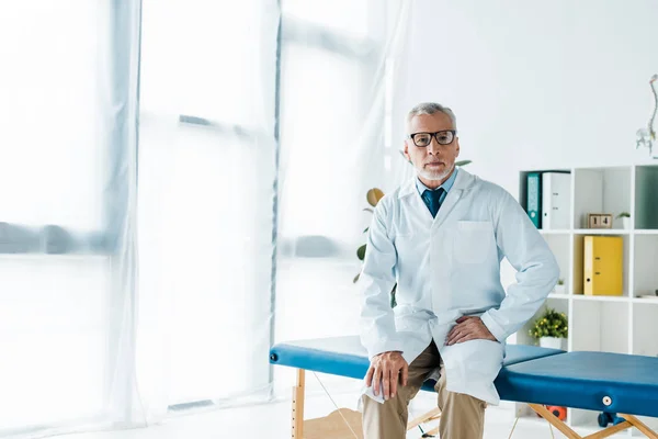 Bearded Doctor Glasses White Coat Sitting Massage Table — Stock Photo, Image