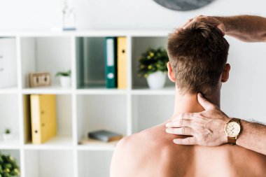 klinikte oturan gömleksiz hastanın boynuna dokunan doktorun kırpılmış görünümü 