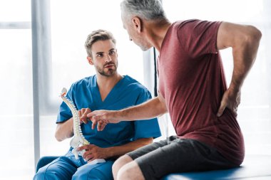 omurga modelini tutan ve geri dokunurken hasta gesturing bakarak doktor seçici odak 