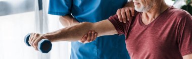klinikte dumbbell ile egzersiz olgun adam yakınında duran doktor panoramik çekim 
