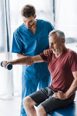 klinikte dambıl ile egzersiz olgun adam yakınında duran doktor 