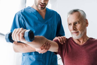 cropped view of doctor standing near mature man holding dumbbell  clipart
