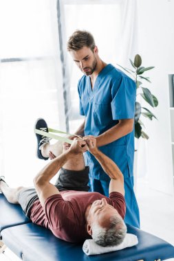 yakışıklı doktor elastik ile egzersiz olgun hastanın bacak tutarak 