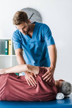 handsome doctor touching mature man lying on massage table  clipart