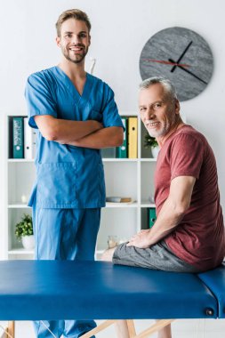 mutlu hasta yakın çapraz kolları ile ayakta neşeli doktor 