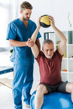 yakışıklı doktor fitness topu egzersiz olgun hasta yakınında duran 