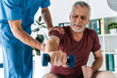 selective focus of mature man working out with dumbbell near doctor  clipart