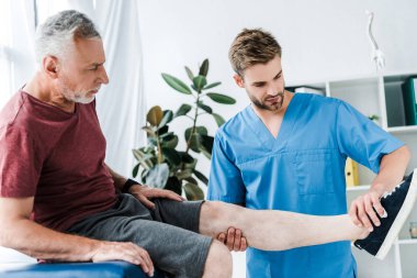klinikte olgun hasta bacak tutan yakışıklı doktor 