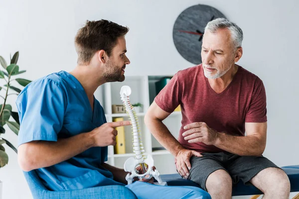 Skäggiga Doctor Pekar Med Fingret Ryggraden Modell Nära Patienten Kliniken — Stockfoto