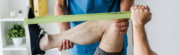 panoramic shot of doctor near man exercising with suspension straps 