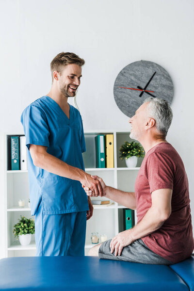 happy doctor shaking hands with cheerful mature patient in clinic 