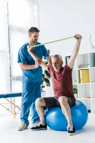 Handsome Doctor Standing Middle Aged Man Exercising Resistance Band While — Stock Photo, Image