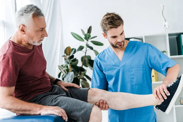 Handsome Doctor Holding Leg Mature Patient Clinic — Stock Photo, Image