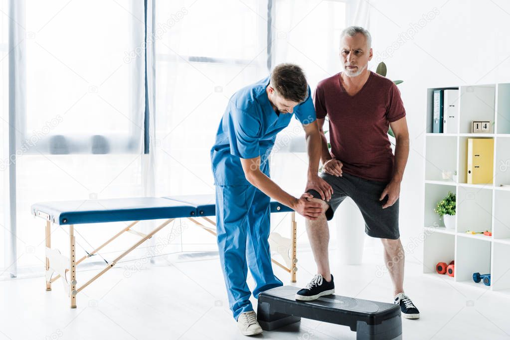handsome doctor touching knee of mature patient on step platform