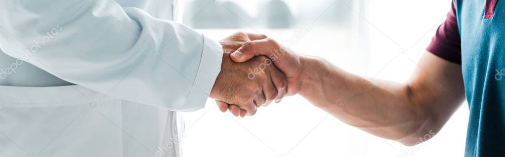 panoramic shot of doctor in white coat shaking hands with man 