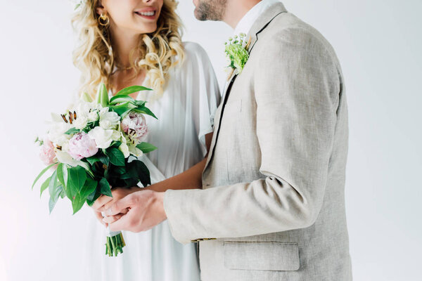 cropped view of bride and handsome bridegroom hugging and holding bouquet