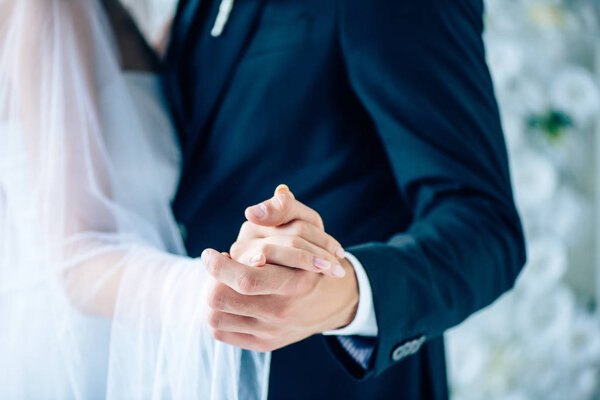 cropped view of bride in wedding dress and bridegroom holding hands 