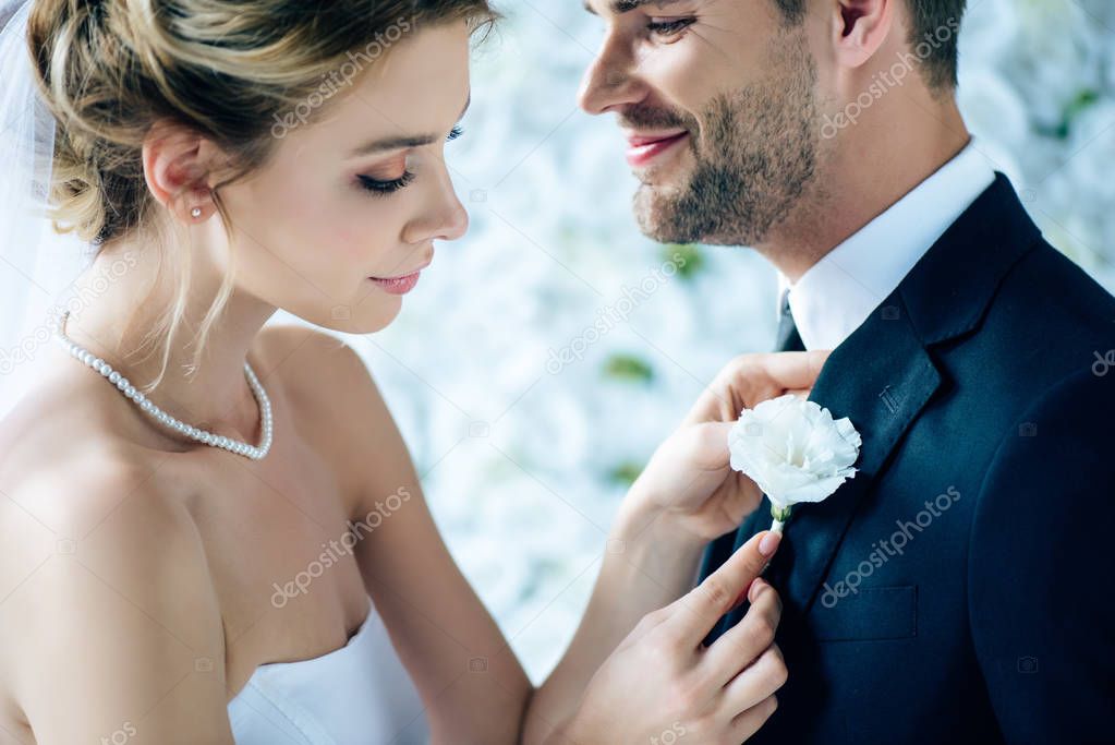 attractive bride in wedding dress holding buttonhole of her bridegroom 