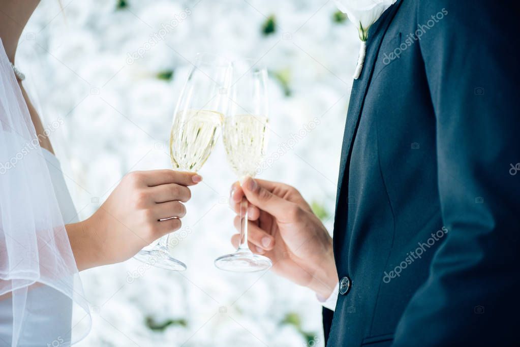 cropped view of bride and bridegroom clinking with champagne glasses