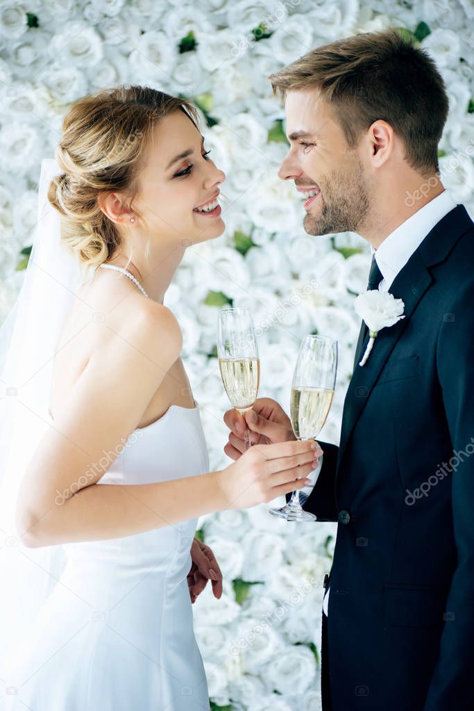 attractive bride and handsome bridegroom smiling and clinking with champagne glasses