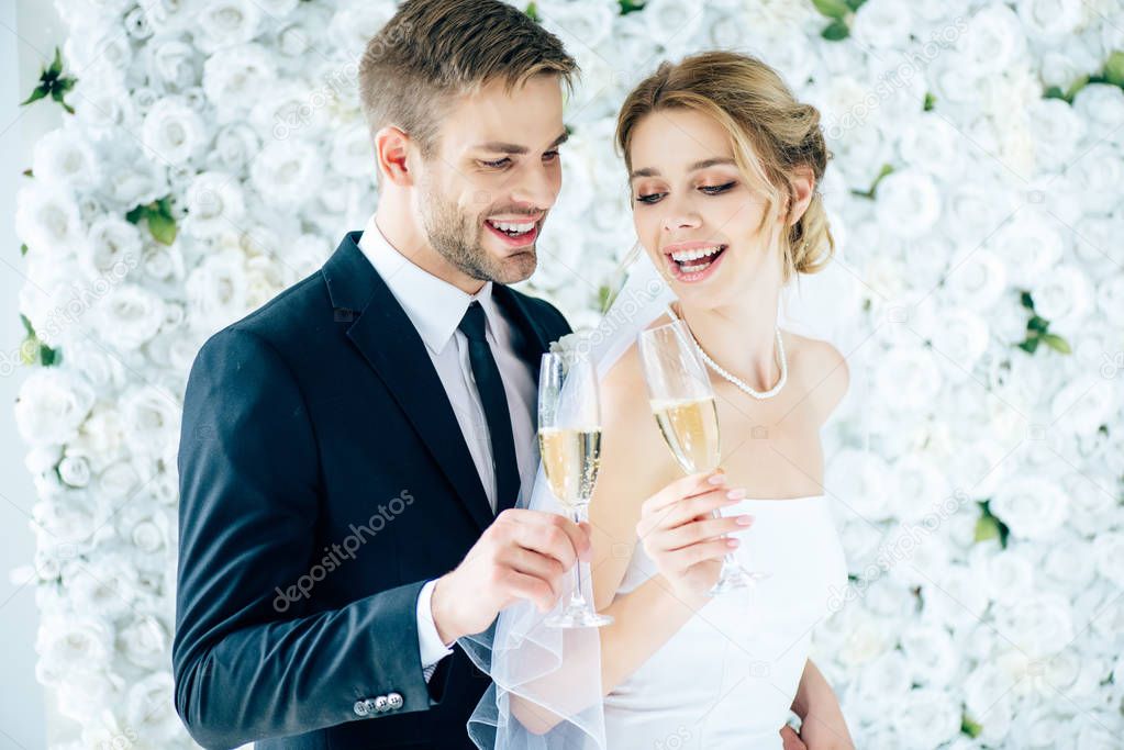 attractive bride and handsome bridegroom smiling and clinking with champagne glasses