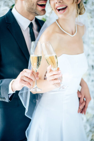 cropped view of bride and bridegroom clinking with champagne glasses
