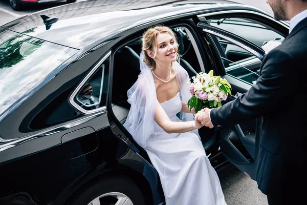 花束で魅力的で笑顔の花嫁に手を与えるスーツの花婿 — ストック写真