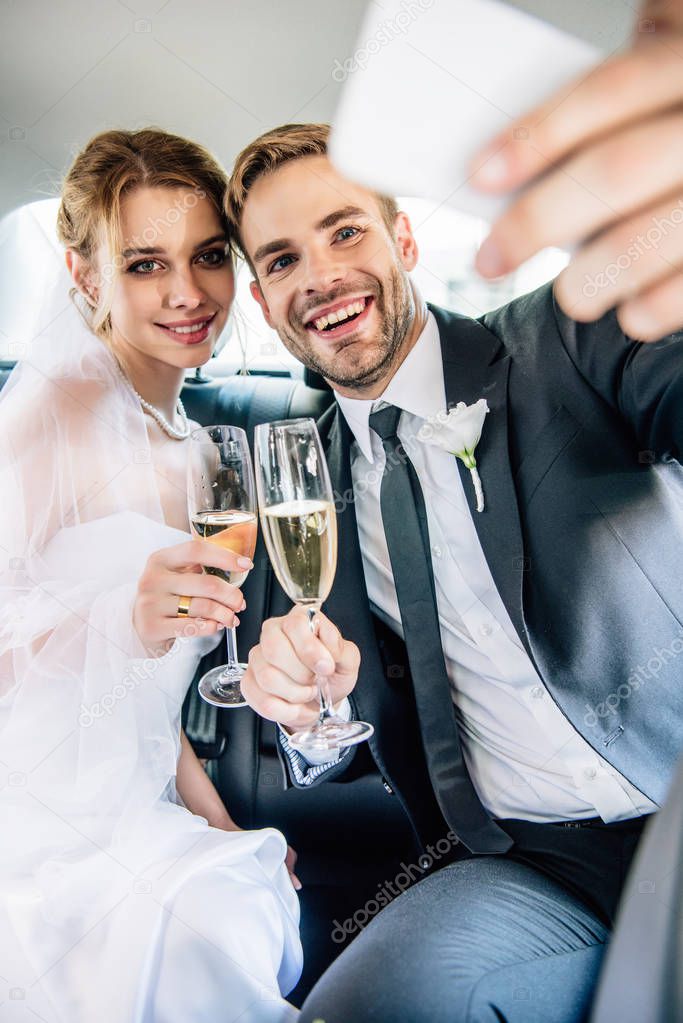 attractive bride and handsome bridegroom taking selfie in car 