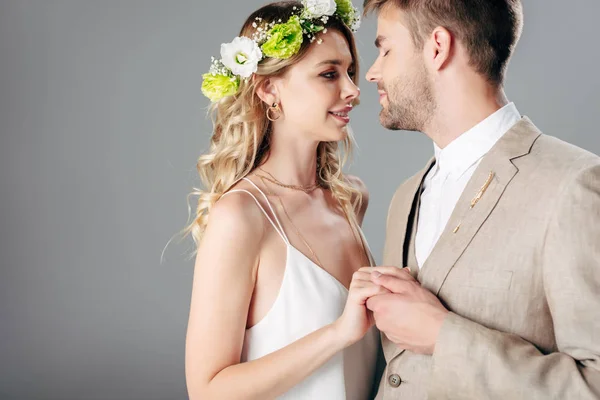 ウェディングドレスで花嫁と抱き合うスーツのハンサムな花婿とグレーに隔離された花輪 — ストック写真