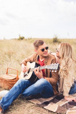 akustik gitar çalan yakışıklı adam ve ona sarılan çekici kadın 