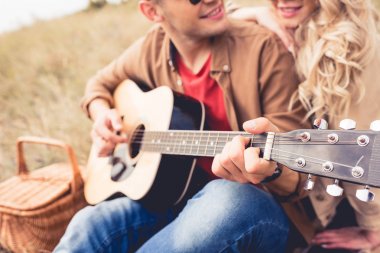 selective focus of man playing acoustic guitar and woman hugging him  clipart