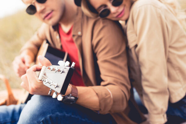 selective focus of man playing acoustic guitar and woman hugging him 