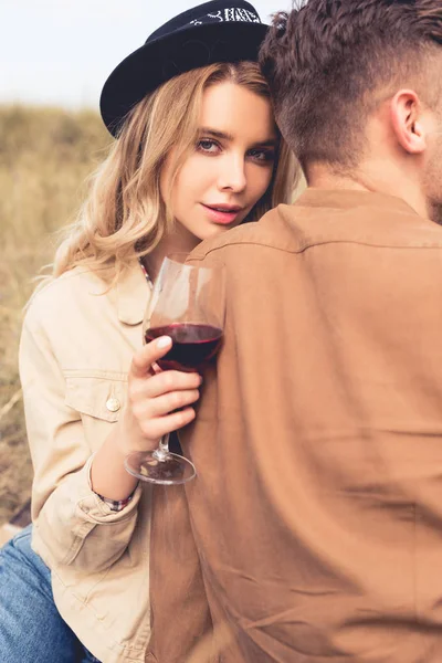 ワイングラスを持ち 男を抱きしめる帽子をかぶった魅力的な女性 — ストック写真