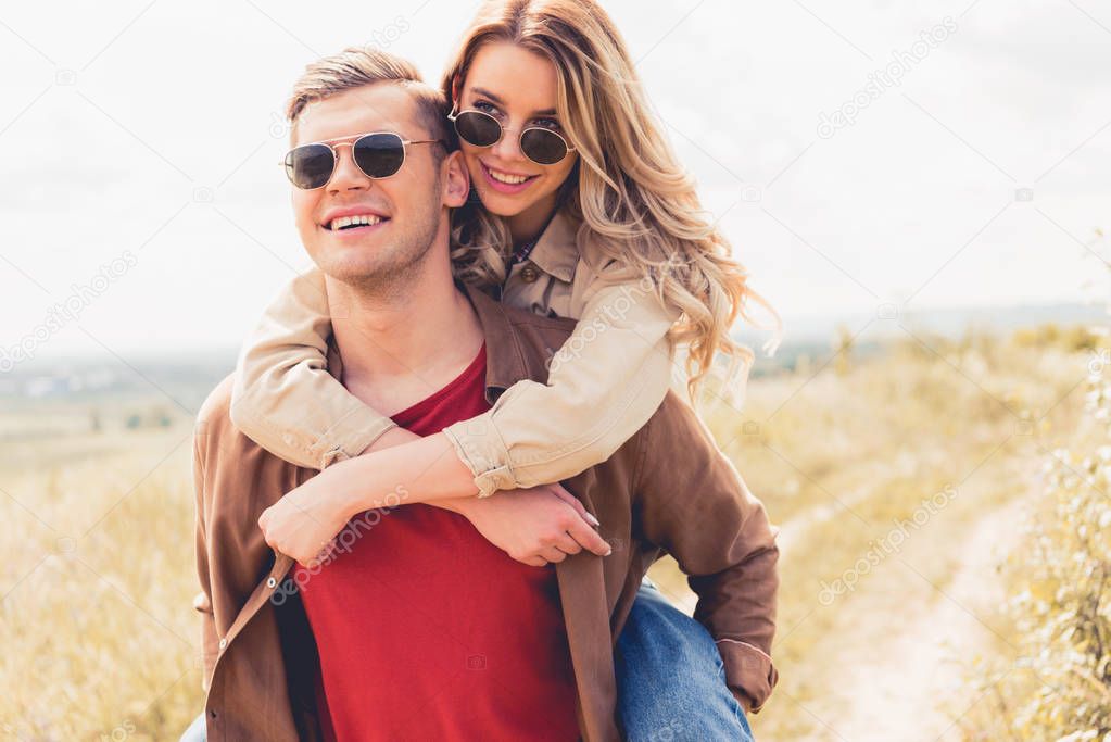 handsome man piggybacking his attractive and blonde girlfriend outside 