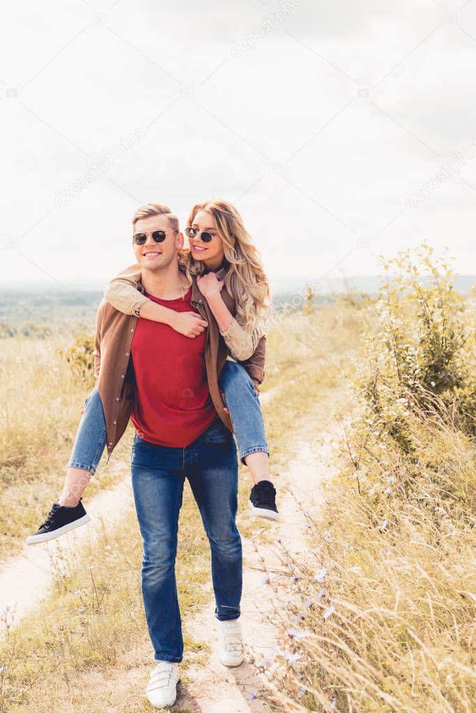 handsome man piggybacking his attractive and blonde girlfriend outside 