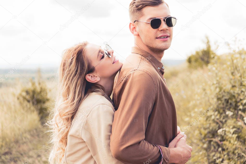 attractive and smiling woman hugging handsome man in sunglasses 