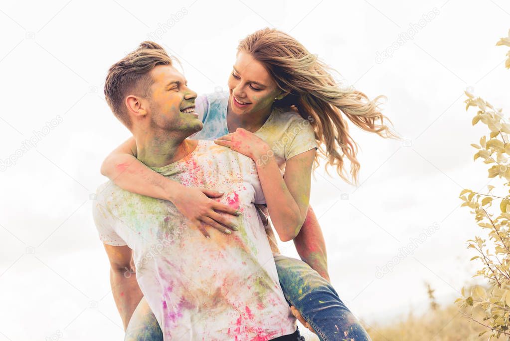 handsome man piggybacking his smiling and attractive girlfriend outside   