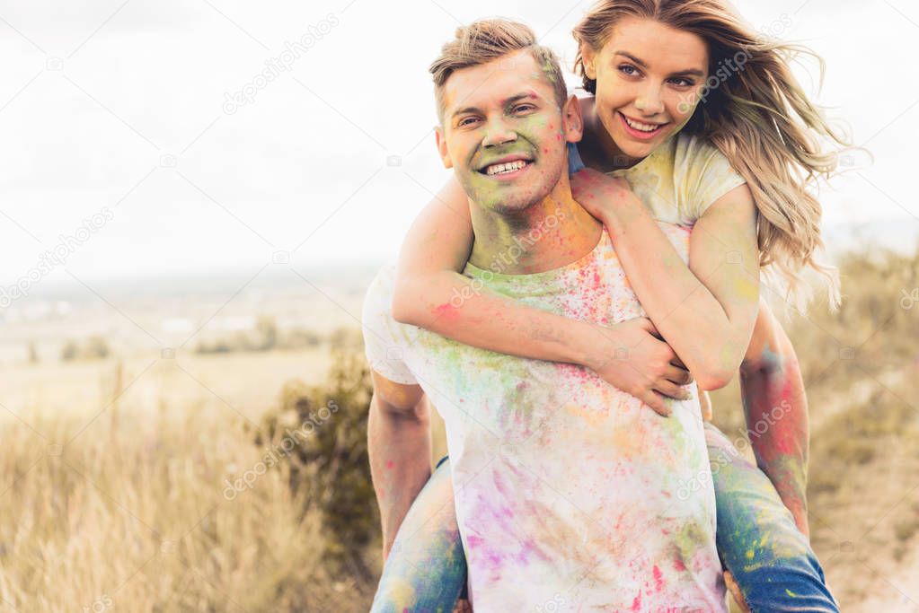 handsome man piggybacking his smiling and attractive girlfriend outside   