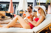 Sexy Paar liegt mit Cocktails auf Liegestühlen im Resort
