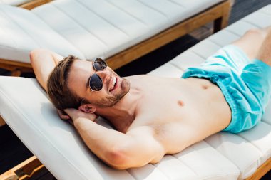 happy shirtless man in sunglasses lying on lounger at resort